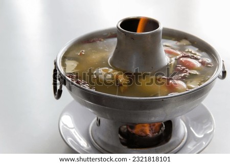 Tom Yum Kung Talay Nam Sai, original recipe, Thai food in a hot pot, ready to be served. The picture is emotional because of the flame. by placing it on a white plate to prevent heat, on a white table