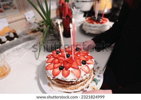 Homemade cake with strawberry for toddler girl with three candles in the hand of elder sister. High quality photo