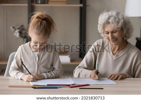 Pleasant old age woman child psychologist doing art therapy session involve little girl patient in drawing picture together. Caring senior grandmother assist preteen grandchild to paint coloring book