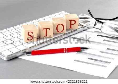 STOP written on wooden cube on the keyboard with chart on grey background