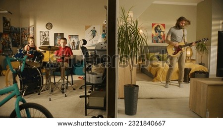 Man plays guitar in bedroom. Young boy plays drum kit and young girl plays ukulele, jumps on bed. View of two rooms or apartments separated by wall. Concept of music, neighbourhood and lifestyle. Royalty-Free Stock Photo #2321840667