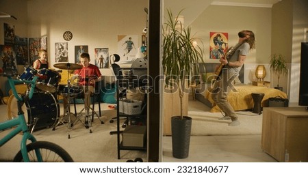 Man plays guitar in bedroom. Young boy plays drum kit and young girl plays ukulele, jumps on bed. View of two rooms or apartments separated by wall. Concept of music, neighbourhood and lifestyle. Royalty-Free Stock Photo #2321840677