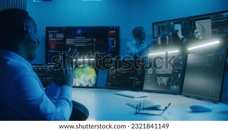 African American flight control employee in headset monitors space mission on multi-monitor computer in command center. Team clap hands after successful space rocket launch displayed on big screens. Royalty-Free Stock Photo #2321841149
