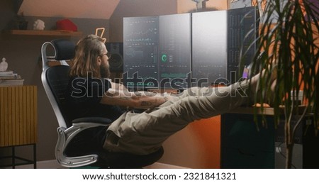 Relaxed male trader watches real-time stocks, exchange market charts on multi-monitor computer workstation, eats fast food. Man works in investment at home office in daytime. Cryptocurrency trading.