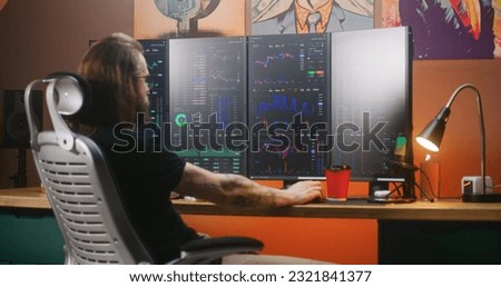Male trader analyzes real-time stocks, exchange market charts on multi-monitor computer workstation, eats delivery food. Man works in investment in cozy room at home office. Cryptocurrency trading.