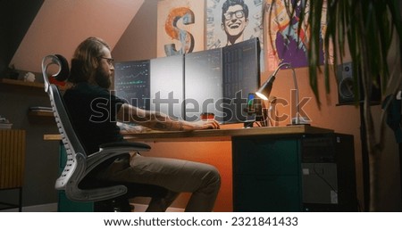 Male financial analyst watches real-time stocks, exchange market charts on multi-monitor computer, eats french fries. Man works in investment in cozy room at home office. Cryptocurrency trading.