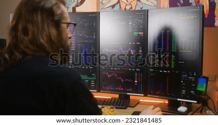 Focused male trader analyzes real-time stocks, exchange market charts on multi-monitor computer workstation, eats fast food. Man works remotely in investment at home office. Cryptocurrency trading.