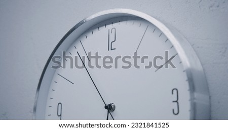 Static shot of white watch with metal frame hanging on the wall and showing time. Walking wall clock in office with modern design. Strict clock with fast running time pointer. Close up. Royalty-Free Stock Photo #2321841525