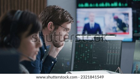 Financial analysts work on multi-monitor computer with real-time stocks and exchange market charts in bank office. Big digital screen showing TV news broadcast. Cryptocurrency trading and analytics.