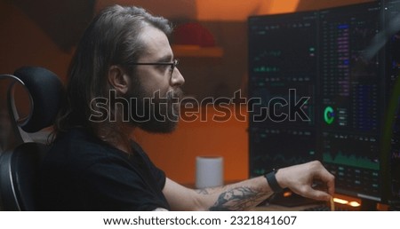 Male trader analyzes real-time stocks, exchange market charts on multi-monitor computer workstation, eats french fries. Man works in investment at home office in the evening. Cryptocurrency trading.