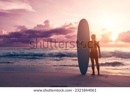 Young man with surfboard on sunset summer tropical beach background.