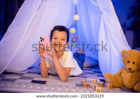 Photo of cute little brother have sleepover party with friends in homemade diy camp playing games on smart gadget