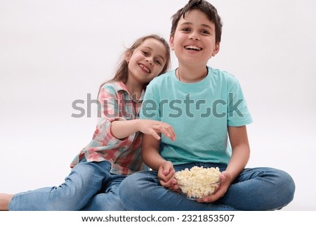 Caucasian amazed funny children, school kids, handsome teen boy and lovely little girl, brother and sister, having fun together, smiling, watching cartoons and eating popcorn. Lifestyle. Entertainment