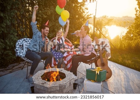 Parents celebrate their daughter's birthday in the backyard. The air is filled with excitement as they blow into colorful party blowers, creating a playful atmosphere. Royalty-Free Stock Photo #2321856017
