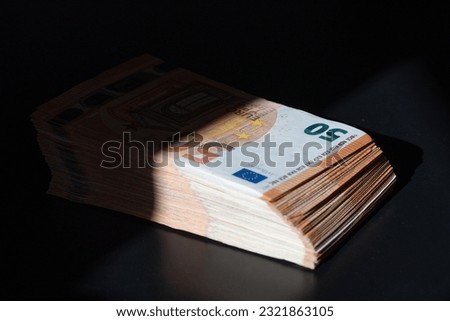 A big wad of money half in the shade on the black table. Euro money banknotes in shadow. 50 euro pack. The concept of the shadow economy. Royalty-Free Stock Photo #2321863105
