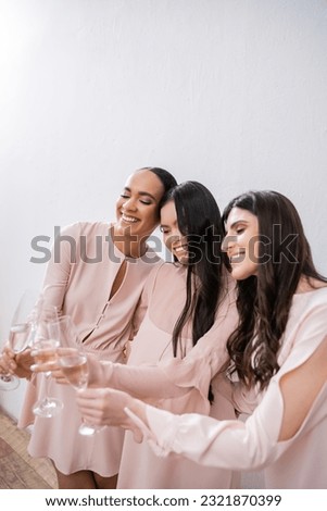 three multicultural bridesmaids, pretty women in pastel pink dresses clinking glasses of champagne on grey background, diversity, fashion, celebration, cheers, diverse races