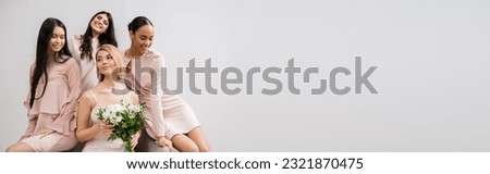 wedding photography, four women, bride with bouquet and bridesmaids, interracial, wedding day, cultural diversity, sitting on armchair, grey background, happiness and joy, wedding dress, banner Royalty-Free Stock Photo #2321870475