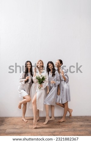 bridal shower, multicultural women holding glasses with champagne, bride with bouquet showing her engagement ring, bridesmaids, diversity, positivity, white flowers, grey background Royalty-Free Stock Photo #2321882367