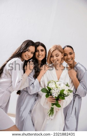 bridal party, four women, joyful bride holding bouquet with white flowers near bridesmaids in silk robes, cultural diversity, togetherness, friendship goals, brunette and blonde women Royalty-Free Stock Photo #2321882431