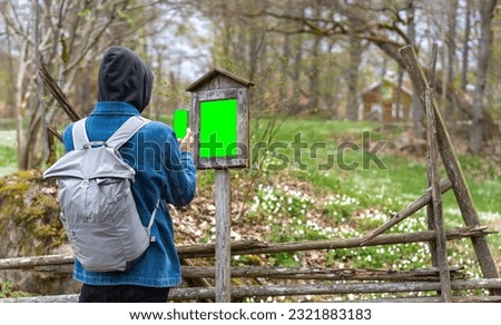 Tourist with backpack search mobile smart phone for information on wooden sign board or take photo of path sign. Tourist attraction description information. Man search for direction. Green screen.