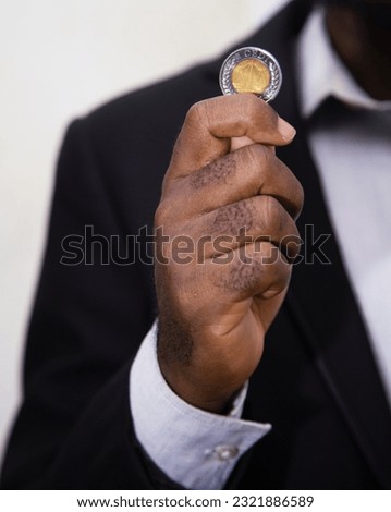 Businessman in suit holding one Ghanaian cedi coin. Hand holding coin