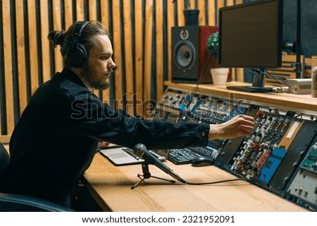 young sound engineer with headphones working in a music studio with monitors and an equalizer mixing mastering tracks