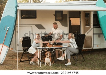 A happy family is resting nearby near their motorhome in the forest. Royalty-Free Stock Photo #2321956745