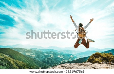 Happy man with backpack jumping on top of the mountain - Delightful hiker with arms up standing over the cliff - Sport and travel life style concept Royalty-Free Stock Photo #2321967569