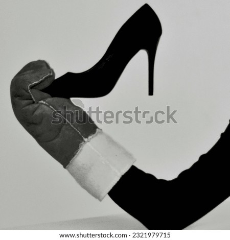 a black female hand in a male winter mitten holds a black female shoe Royalty-Free Stock Photo #2321979715