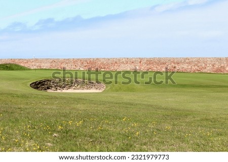 An incredible view of a classic links golf hole with ancient stone walls in Scotland with the ocean in the background in Dunbar, in the East Lothian region of Scotland 