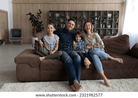 Portrait of overjoyed young Caucasian family with teen children relax on sofa in modern new living room. Smiling parents with teenage kids renters on couch at home. Rent, relocation, moving concept.