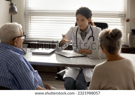 Young Caucasian female doctor in white medical uniform talk consult middle-aged old couple in private hospital. Woman GP or therapist have consultation in clinic with elderly man and woman patients. Royalty-Free Stock Photo #2321988057
