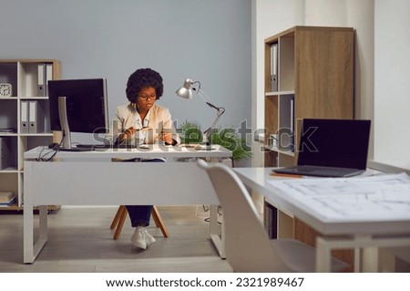 Young african american woman auditor checking financial documents with magnifying glass over office desk. Fraud investigation and tax audit. Accountant searching information in document. Royalty-Free Stock Photo #2321989467