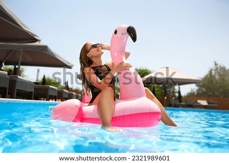 Hot slim woman having fun laughing on inflatable pink flamingo float mattress in bikini at swimming pool. Attractive fit girl in swimwear lies in the sun on floaty. Pretty female on tropical vacation.