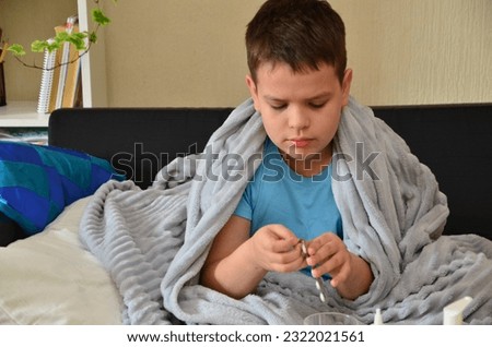Sick child boy lying in bed with a fever, resting at home. a boy with a cold, treated. medicines, throat and nose spray. sick kid with runny nose and fever heat lying on couch. drinking a hot drink.