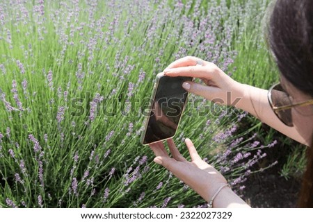 Young woman takes a picture of lavender flowers on a field with a smartphone.