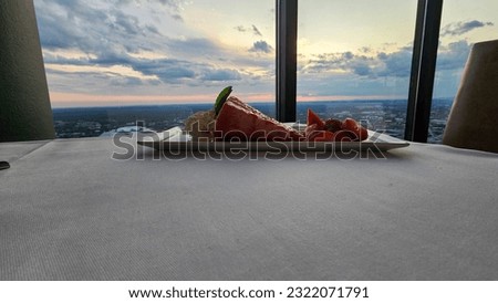 A plate of strawberry short cake with sliced strawberries on a table with a white tablecloth and a gorgeous view of the city skyline at sunset in at The Sun Dial Restaurant in Atlanta Georgia USA