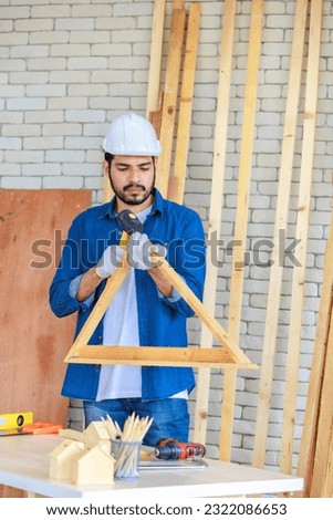 Asian Indian professional male engineer architect foreman labor worker wears safety goggles and gloves using square degree angle steel ruler measuring triangle wood plank in home construction site. Royalty-Free Stock Photo #2322086653