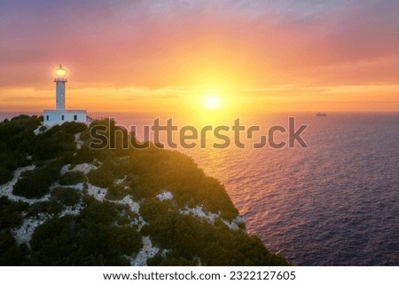 Captivating sunset over the gleaming white lighthouse perched on Cape Ducato, Lefkada, Greece. Majestic lighthouse atop a cliff, with the sun gently caressing the sea in the backdrop
