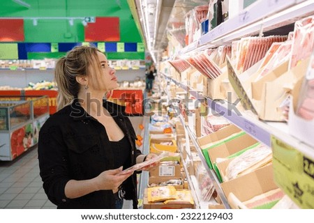 A happy young woman is pushing a shopping cart filled with groceries, a sign of a successful shopping trip at the local market.
