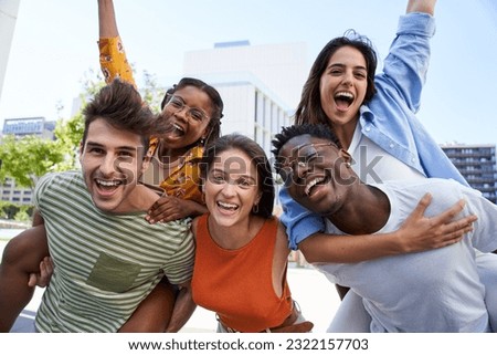 Portrait of happy young friends looking at camera excited. Smiling group of classmates having fun together outdoors. Crazy community of college students. Multicultural people hugging and piggyback. Royalty-Free Stock Photo #2322157703