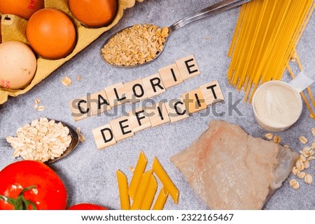 the inscription calorie deficit next to healthy food products. Flat lay photo showing weight loss and getting in shape Royalty-Free Stock Photo #2322165467