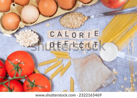 the inscription calorie deficit next to healthy food products. Flat lay photo showing weight loss and getting in shape Royalty-Free Stock Photo #2322165469