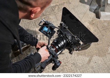 a professional cameraman holds a video camera from the floor level and shoots a lower angle. looking at camera monitor