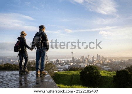 Couple standing on Mt Eden summit and watching sunrise over Auckland city. Selective focus on people in foreground.  Royalty-Free Stock Photo #2322182489