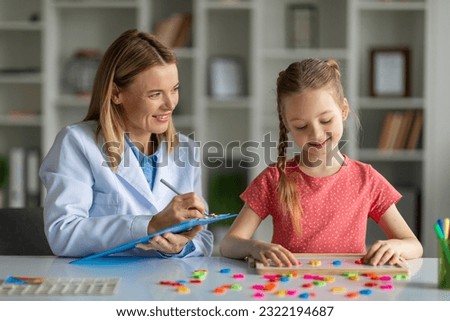 Assessment of kids mental development. Woman psychologist watching little girl playing with logical game, evaluating readiness for elementary school, child making words of colorful letters Royalty-Free Stock Photo #2322194687