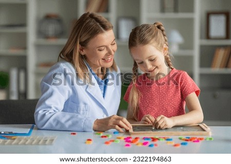 Cute Little Girl Painting On Mini Chalkboard During Meeting With Child Development Specialist At Office, Therapist Lady Testing Smiling Female Child, Evaluating Readiness For Elementary School Royalty-Free Stock Photo #2322194863