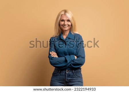 Stylish confident adult 50 years old attractive blonde woman standing arms crossed looking at camera at beige background. Portrait of sophisticated senior lady advertising products and services Royalty-Free Stock Photo #2322194933