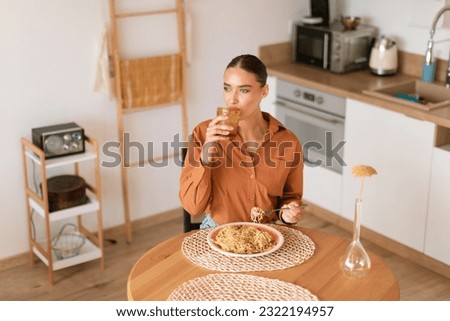 Young caucasian woman taking sip of water during dinner of home cooked pasta while sitting at table in cozy kitchen interior, above view, free space Royalty-Free Stock Photo #2322194957