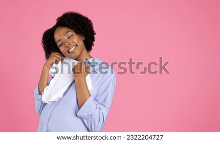 Happy millennial african american curly pregnant woman in casual hug baby clothes, enjoy future motherhood, isolated on pink studio background. Shopping, buy for kid, expect child